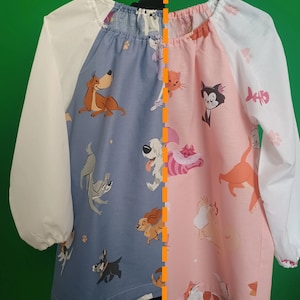 Könnte beinhalten: Ein langärmliges Hemd in Blau und Rosa mit weißem Kragen und Manschetten. Das Hemd hat ein Muster mit Cartoon-Hunden und -Katzen auf der Vorderseite. Das Hemd ist in der Mitte geteilt, eine Seite ist blau und die andere Seite rosa.