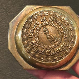 May include: Vintage brass belt buckle with an octagonal shape. The center features a circular design with the words "Board of Education" and "Greater Chicago" surrounding a hand holding a torch within a laurel wreath.