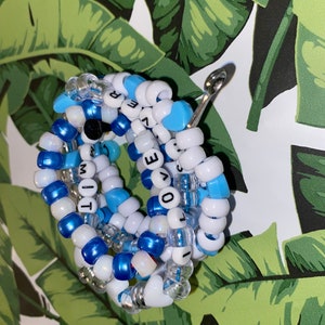May include: A close-up of a beaded bracelet with the words "I LOVE YOU" and "MIT" spelled out in black letters on white beads. The bracelet is made with blue, white, and clear beads.
