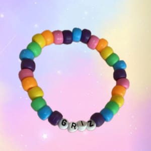 Pode incluir: Um bracelete de contas coloridas do arco-íris com o nome "GRIZ" escrito em contas brancas.