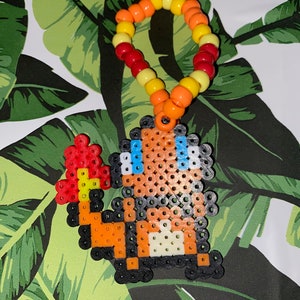 May include: A beaded bracelet with red, orange, and yellow beads, with a pixelated image of a cartoon character with orange, black, and white colors attached to the bracelet.