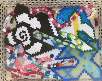 Peut inclure: Un panier en osier blanc rempli de bracelets et de colliers en perles de pixels colorés. Les bracelets et les colliers présentent divers motifs, notamment des lettres, des cœurs et des formes géométriques. Les perles sont en plastique et se déclinent en une variété de couleurs, notamment le bleu, le vert, le jaune, le rose, le rouge et le blanc.