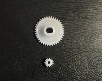 May include: Two white plastic gears, one larger than the other. The larger gear has a central hole.