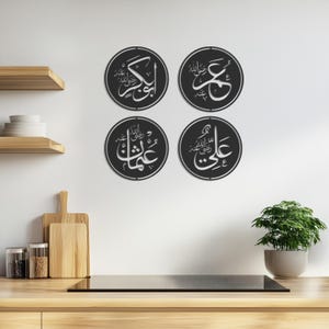 May include: Four black circular wall decor pieces with white Arabic calligraphy. Each piece features a different name in Arabic script.