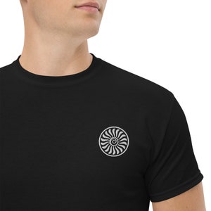 Puede incluir: Una camiseta negra con un diseño bordado blanco de un motor a reacción estilizado.