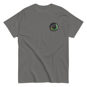 May include: A dark gray t-shirt with a small, round, black and white gauge printed on the left chest. The gauge has a green, yellow, and red arc with numbers and markings.
