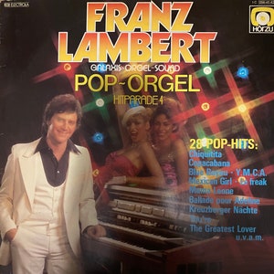 May include: A vintage vinyl record cover featuring a man in a white suit playing a keyboard with two women in the background. The cover is titled "Franz Lambert Pop-Orgel Hitparade 4" and lists 28 pop hits including "Chiquitita", "Copacabana", "Blue Bayou", "Y.M.C.A.", "Mexican Girl", "Le Freak", "Mama Leone", "Ballade pour Adeline", "Kreuzberger Nächte", "The Greatest Lover", and "u.v.a.m."
