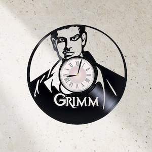 May include: Black vinyl record clock featuring a silhouette of a man's face with a clock face in the center. The clock face has Roman numerals and a pink background. The text "GRIMM" is printed below the clock face.