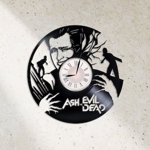 Könnte beinhalten: Schwarze Schallplattenuhr mit einer Silhouette von Ash Williams aus der Evil Dead-Reihe. Das Zifferblatt der Uhr ist weiß mit schwarzen römischen Ziffern als Stundenmarkierungen und einem rosafarbenen Zentrum. Der Text "Ash vs Evil Dead" ist unterhalb des Zifferblatts gedruckt.