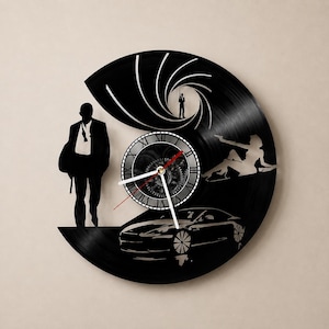 May include: A circular wall clock crafted from a black vinyl record featuring laser-cut silhouettes of a man in a suit, a sports car, a reclining figure, and a gun barrel motif. The center displays a clock face with Roman numerals and white hands.