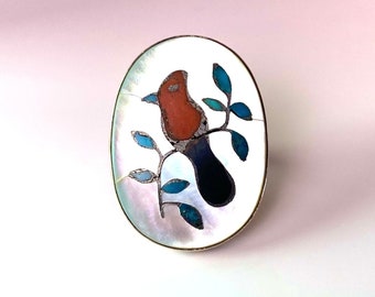 Statement ring of cardinal sitting on leafy branch set in large oval of Mother of Pearl inlay. May be Zuni inlay ring.