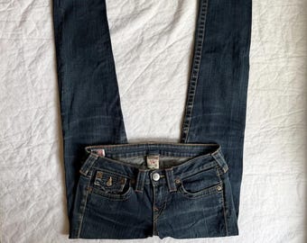 May include: Dark blue denim jeans featuring a classic five-pocket design, a button fly closure, and prominent contrast stitching. These slim-fit jeans include a small coin pocket with a button flap and a branded interior label at the waistband.