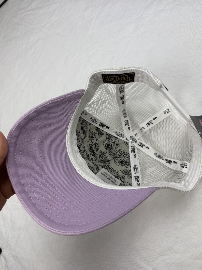 May include: A lavender baseball cap with a white mesh back and a curved brim. The interior features a patterned lining and white straps. The Von Dutch logo is visible on the label.