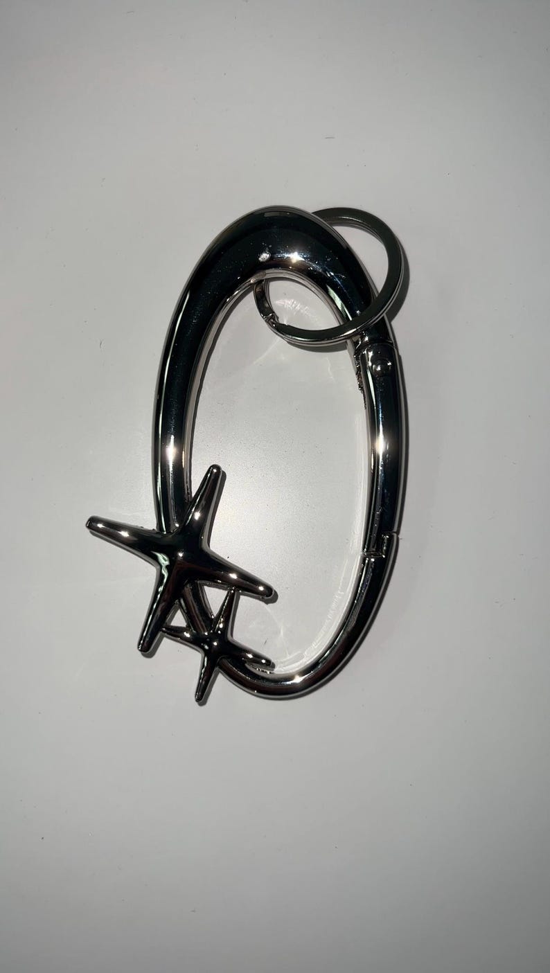 Peut inclure: Un porte-cl&eacute;s en m&eacute;tal argent&eacute; avec un grand anneau ovale et un charme en forme d'&eacute;toile. Le charme est compos&eacute; de deux &eacute;toiles qui se chevauchent.