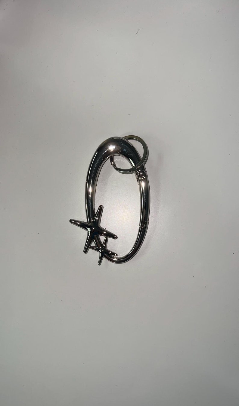 Peut inclure: Un porte-cl&eacute;s en m&eacute;tal argent&eacute; avec un motif d'&eacute;toile. Le porte-cl&eacute;s a un grand anneau ovale et un anneau plus petit pour attacher les cl&eacute;s.