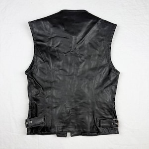 May include: Black leather vest with a classic design. Features a V-neck, sleeveless cut, and adjustable buckles at the waist. The vest has a smooth, slightly textured surface and a tailored fit. A timeless piece for a variety of styles.