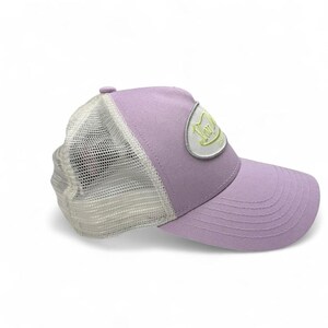 May include: A lilac trucker cap with a white mesh back and a curved peak. The cap has a patch with text in a light green colour. A casual accessory.