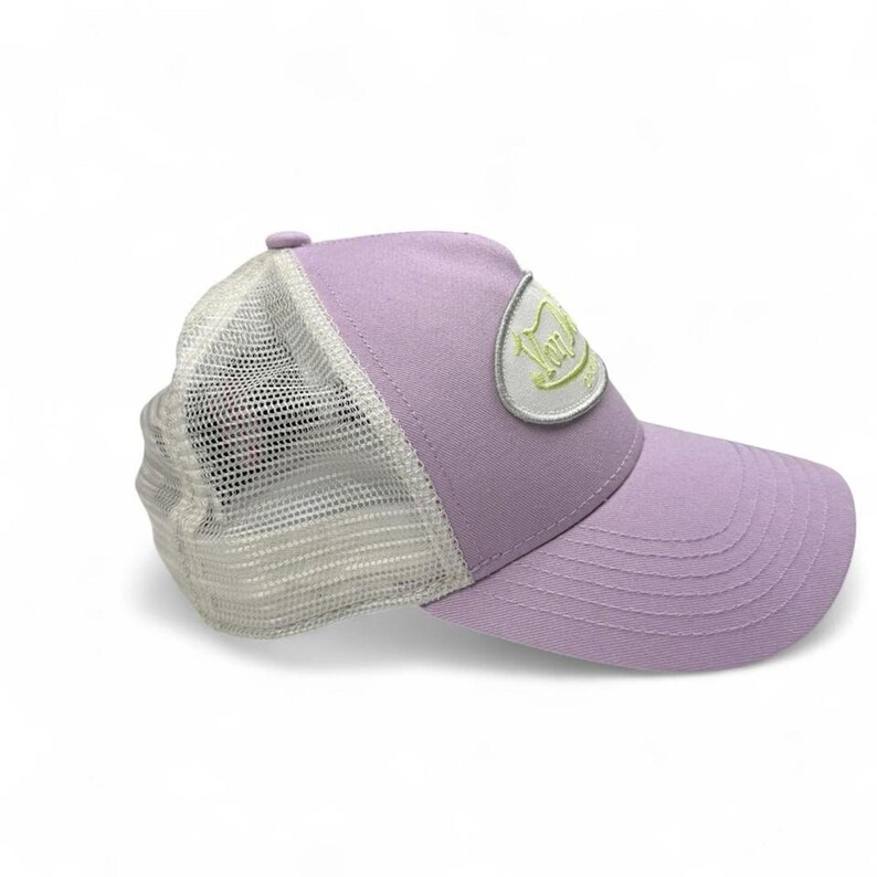 May include: A lilac trucker cap with a white mesh back and a curved peak. The cap has a patch with text in a light green colour. A casual accessory.