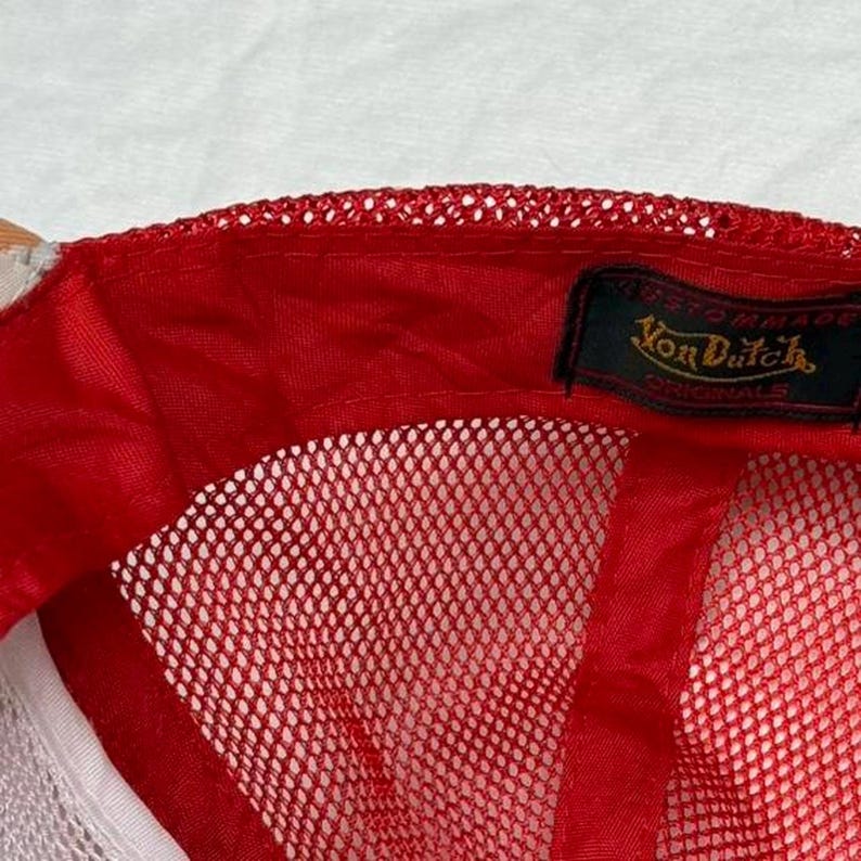 May include: Red and white trucker hat with a mesh back and a curved brim. The hat features a red front panel and a white mesh back. The Von Dutch logo is visible on a black label.