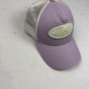 May include: A lavender baseball cap with a mesh back and a curved peak. The cap has the embroidered text "Von Dutch Originals" in light green on a white oval patch.
