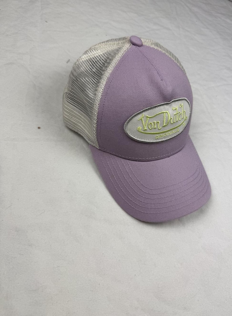 May include: A lavender baseball cap with a mesh back and a curved peak. The cap has the embroidered text "Von Dutch Originals" in light green on a white oval patch.