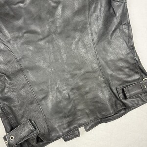 May include: Black leather vest with a perforated design. The vest features a classic biker style with a tailored fit, visible stitching, and adjustable side straps with metal buckles. A timeless piece for a rugged look.