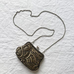 May include: A vintage beaded evening bag with a silver chain strap. The bag features an ornate design with gold and bronze beads on a satin background. The clasp is silver.