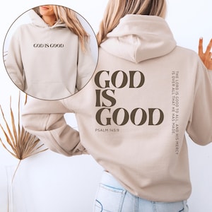 May include: A beige hoodie with the text "GOD IS GOOD" on the front and back. The back of the hoodie also features the text "GOD IS GOOD" in a larger font, along with "PSALM 145:9" and a quote.