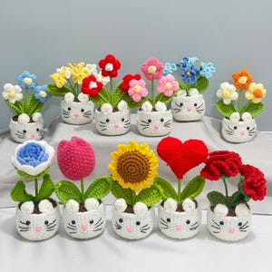 May include: A collection of handmade crochet flowers in white bunny-shaped pots. The flowers are various colors, including blue, yellow, red, pink, and orange. The pots have black embroidered whiskers and eyes. The arrangement includes a sunflower, a heart, and a rose.
