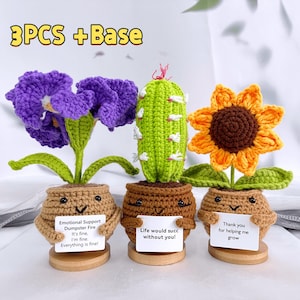 May include: Crocheted flower set with a purple iris, green cactus, and orange sunflower. Each flower is in a brown pot with a smiling face and a small sign. The text "3PCS + Base" is at the top.