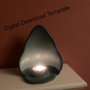 Puede incluir: Un portavelas de cerámica de color verde azulado con una vela de té encendida. El soporte tiene una forma orgánica única y está colocado sobre una superficie blanca. Las palabras "Digital Download Template" están impresas en la esquina superior izquierda.