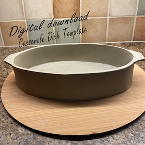 Pode incluir: Um prato de cerâmica cinza claro com bordas arredondadas e duas alças. O prato está sobre uma tábua de cortar redonda de madeira. O texto "Download digital Modelo de prato para assar" está escrito em itálico preto acima do prato.