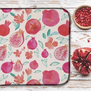 May include: A rectangular kitchen mat featuring a watercolour design of pomegranates and flowers in red, pink, and orange hues. The mat sits on a white wooden surface, with a bowl of pomegranate seeds and a cut pomegranate.