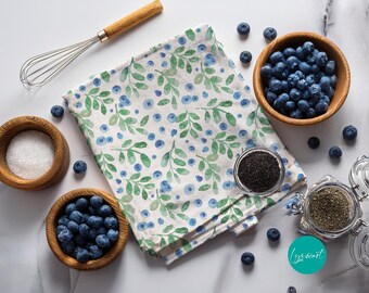 Può includere: Un canovaccio da cucina bianco con un motivo ad acquerello di foglie verdi e mirtilli blu. Il canovaccio è circondato da ciotole in legno riempite di mirtilli freschi e zucchero bianco, una frusta in metallo e barattoli di vetro con spezie.