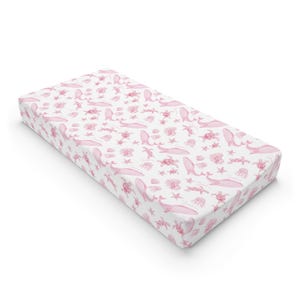 May include: A rectangular crib sheet featuring a repeating pattern of light pink marine life illustrations, including whales, sea turtles, jellyfish, starfish, and seashells, set against a solid white background on a fitted mattress cover.