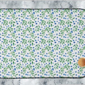 Puede incluir: Una estera de secado de platos blanca con un patrón repetitivo de hojas verdes y arándanos azules. La estera tiene un borde gris oscuro.