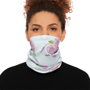 Puede incluir: Una mascarilla facial azul claro con un patrón floral con rosas rosas y hojas verdes. La mascarilla está hecha de un tejido suave y transpirable y está diseñada para ser cómoda de llevar.