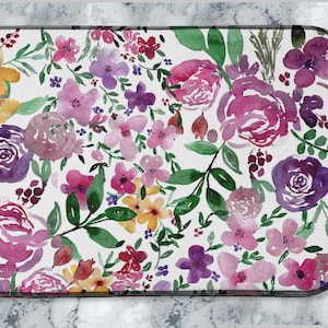 May include: Rectangular floral bath mat with a watercolour design. The mat features a white background decorated with various flowers in shades of pink, purple, yellow, and green. The mat's dimensions are not visible.