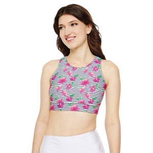 Op de afbeelding: Een mouwloze sport-bh met een bloemenpatroon van roze bloemen op een gestreepte achtergrond van marineblauw en wit. De bh is een crop top-stijl, met een hoge halslijn en een racerback-ontwerp.