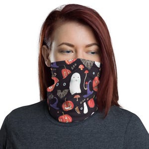 Könnte beinhalten: Schwarzer Mund-Nasen-Schutz mit Halloween-Muster. Das Design umfasst orangefarbene Kürbisse, weiße Geister, lila Hexenhüte und braune Pilze. Das Wort "boo" ist ebenfalls sichtbar. Der Mund-Nasen-Schutz wird von einer Person getragen.