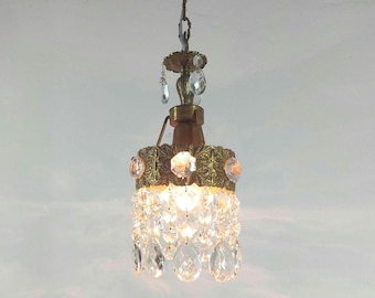 May include: A gold-toned chandelier with crystal drops and a decorative floral design. The chandelier has a single light bulb and is hanging from a chain.