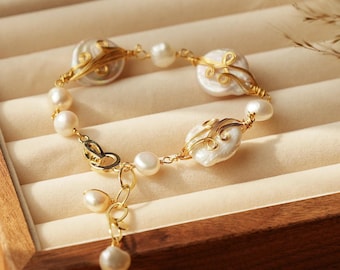 Puede incluir: Un delicado brazalete de oro con un diseño de perlas y alambre. El brazalete presenta tres perlas grandes e irregulares envueltas en alambre de oro con intrincados patrones. Perlas más pequeñas están enhebradas entre las más grandes. El brazalete tiene una cadena de oro con un pequeño dije de perla.