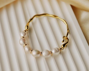 May include: A gold bracelet with a unique, irregular shape and a row of white pearls.