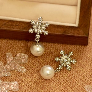 May include: A pair of silver snowflake earrings with a pearl drop. The snowflakes are made of clear rhinestones and the pearls are white.