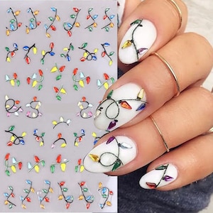 May include: A sheet of colorful nail stickers featuring a string of Christmas lights. The stickers are on a white background and are perfect for adding a festive touch to your nails.