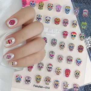 May include: Nail art stickers featuring colorful sugar skull designs. The stickers are in various colors and patterns, with examples applied to fingernails. The sheet of stickers has the text "THE SKULL Fairyfair" and "Fairyfair-014".