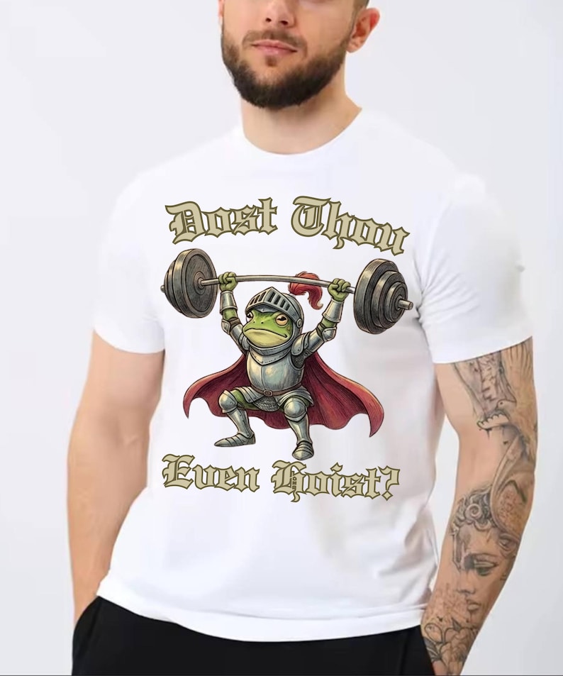 Pu&ograve; includere: T-shirt bianca con un ranocchio dei cartoni animati in armatura da cavaliere che solleva un bilanciere. La rana &egrave; verde con un mantello rosso e un elmo argentato. Il testo sulla maglietta recita "Dost Thou Even Hoist?"