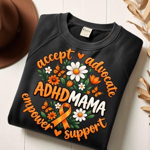以下が含まれることがあります： オレンジと白の文字でADHDMAMAと書かれたグラフィックが特徴の黒いスウェットシャツ。デザインには、オレンジ色の蝶、白いデイジー、オレンジ色の花、緑の葉、そしてaccept、advocate、empower、supportという言葉が添えられたオレンジ色の啓発リボンが含まれています。