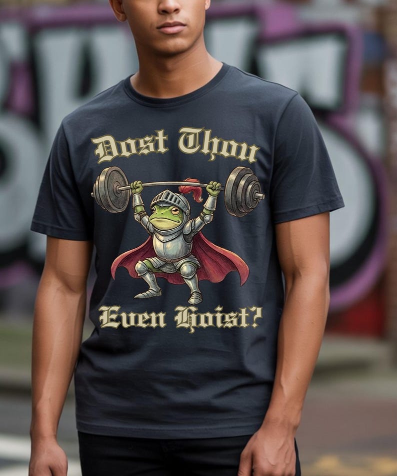 Pu&ograve; includere: T-shirt blu navy scuro con un ranocchio dei cartoni animati in armatura da cavaliere che solleva un bilanciere. Il testo "Dost Thou Even Hoist?" &egrave; stampato sopra e sotto l'illustrazione della rana in oro.