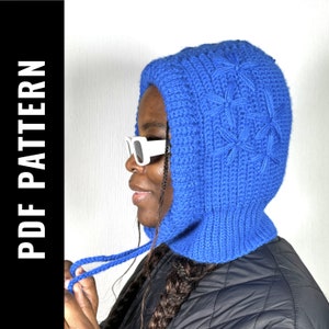 Puede incluir: Un gorro de punto azul con capucha y un patrón de estrellas. El gorro tiene una larga corbata que se puede atar debajo de la barbilla.